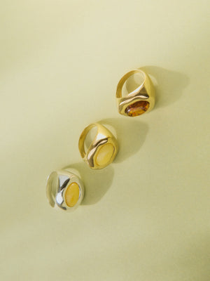 Three gold and silver rings set with cognac and milky yellow Baltic amber on a pale green background