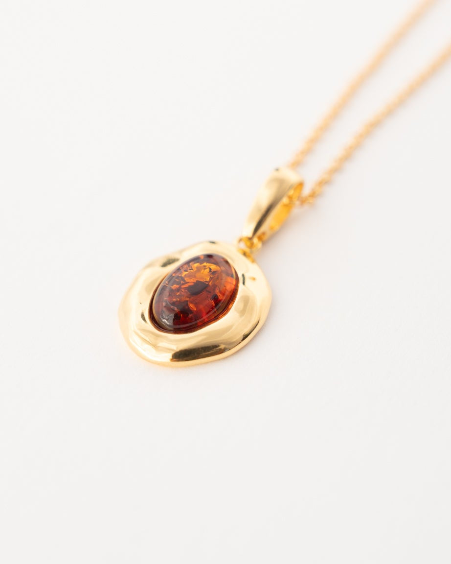 A gold pendant necklace featuring an oval amber stone, displayed on a clean white background.
